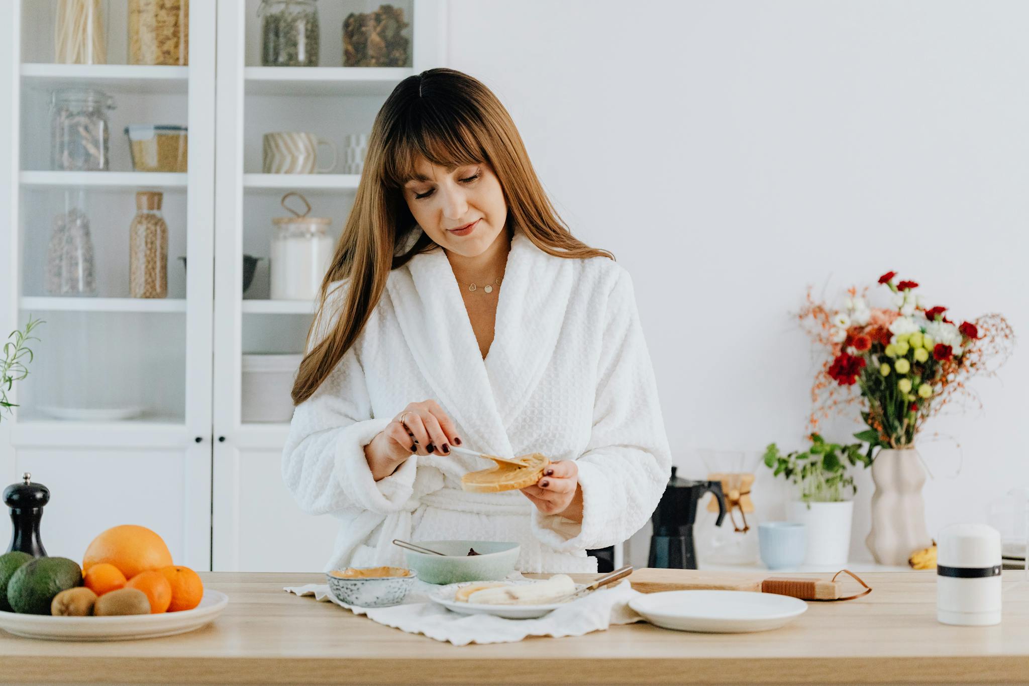 A woman in a bathrobe preparing breakfast in a home kitchen.