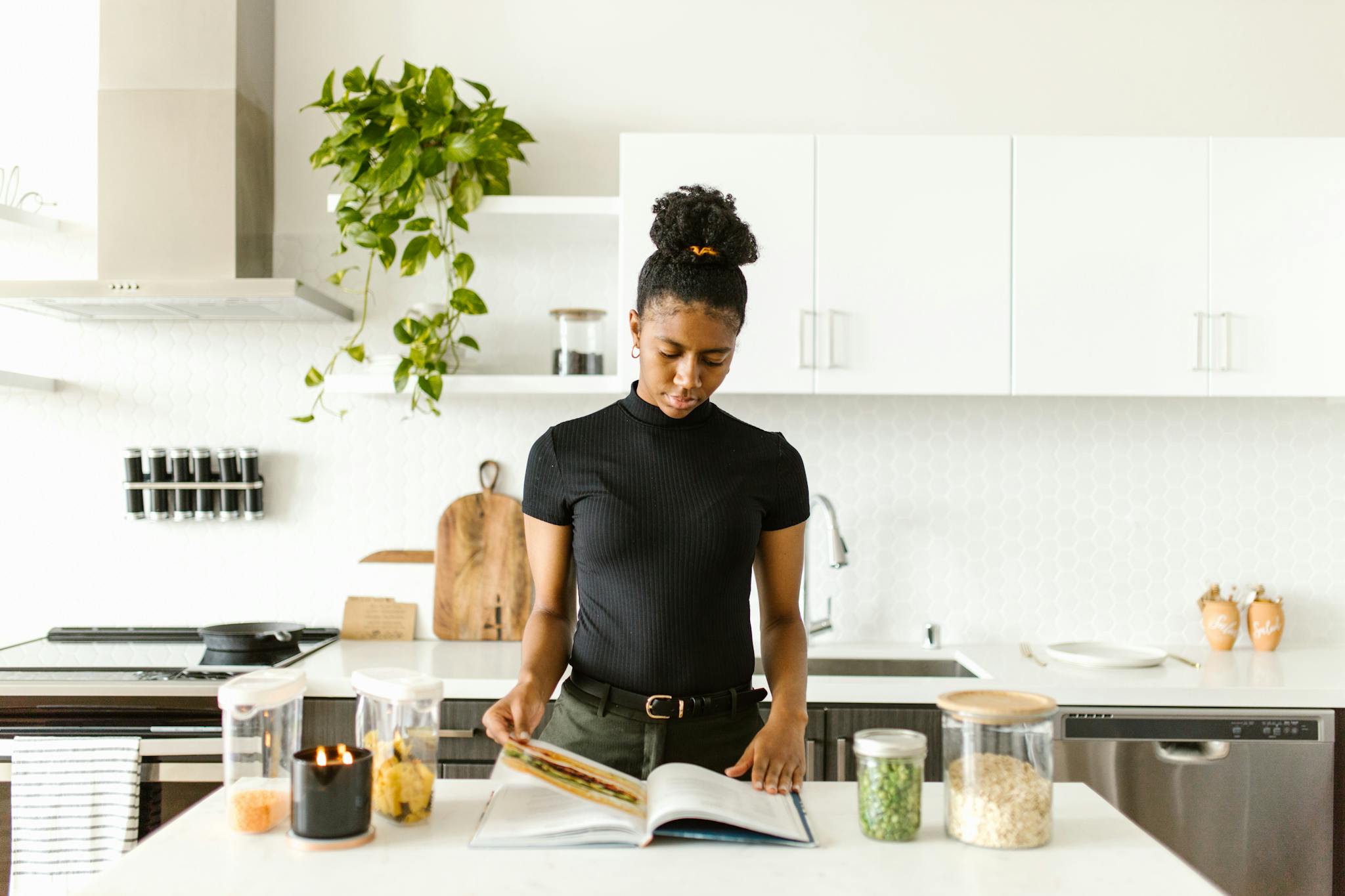 A woman in black top reading a book in a well-lit modern kitchen setting.