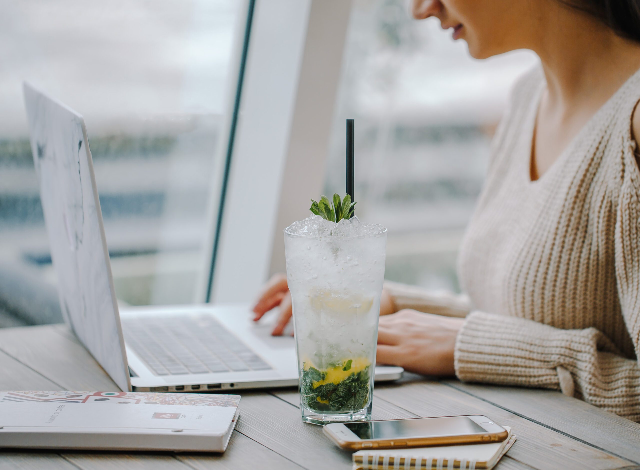 mojito glass next to woman working on notebook near the window how to be more productive at home