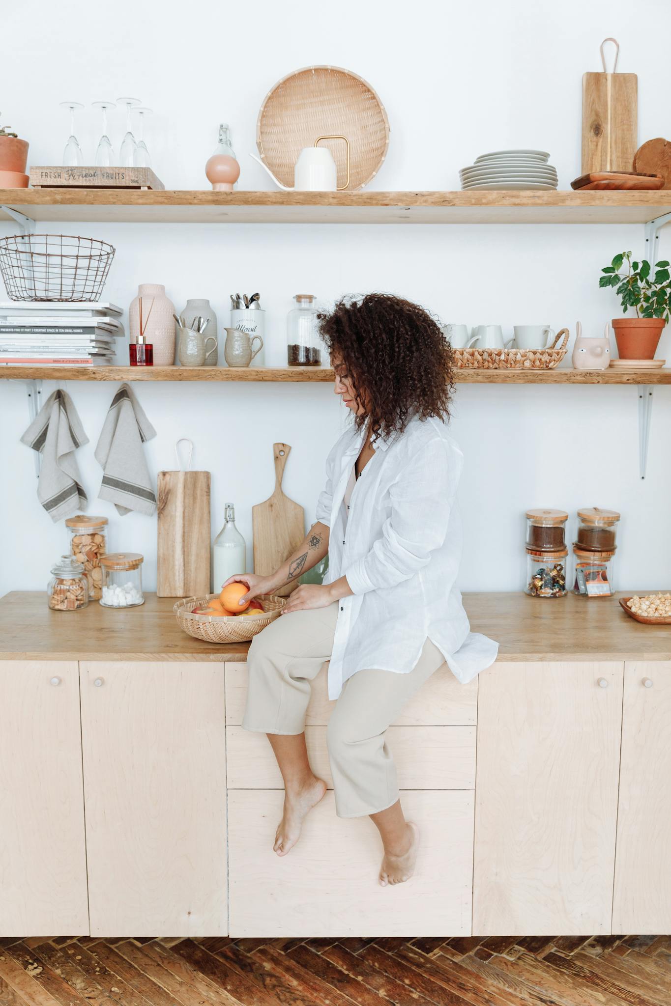 Woman sitting on a kitchen counter arranging fruit, creating a cozy and organized kitchen space.